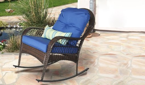 Navy-cushioned wicker rocker on a stone patio beside a pond